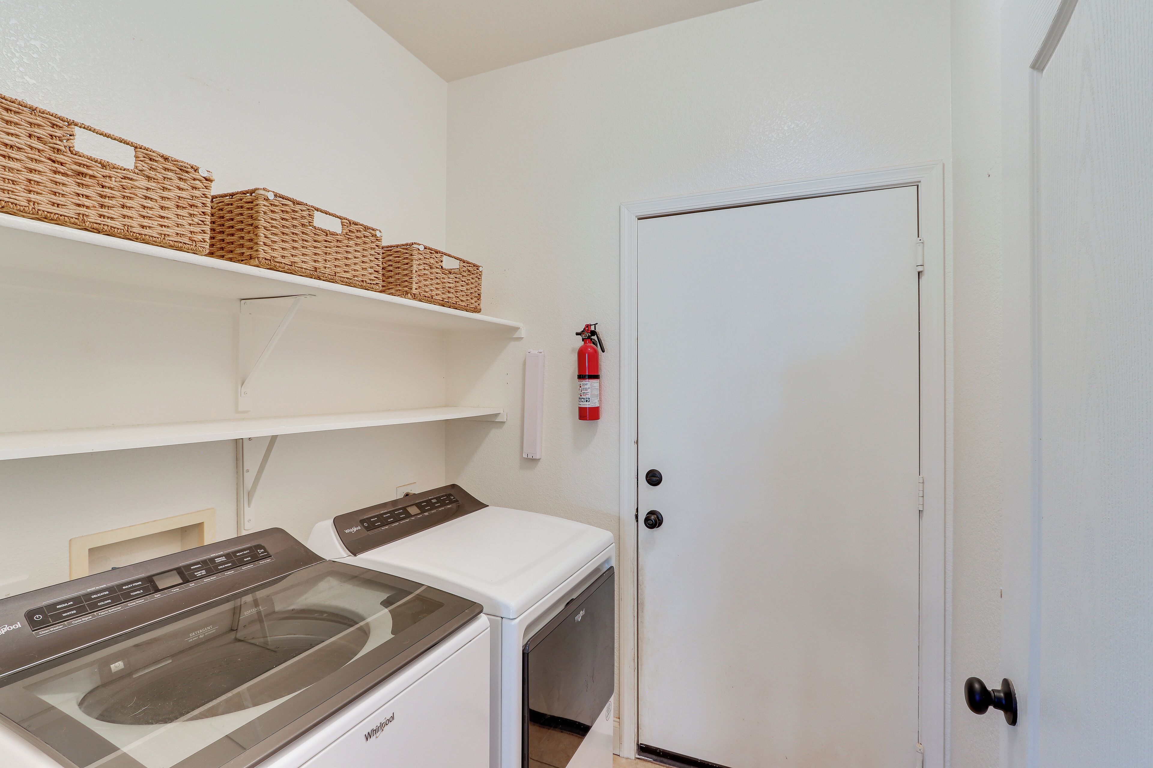 A laundry room with a washing machine, dryer, shelves with baskets, and a fire extinguisher.