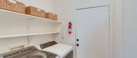 A laundry room with a washing machine, dryer, shelves with baskets, and a fire extinguisher.