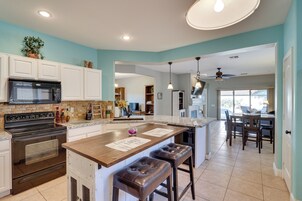 Una cocina con una isla central, muebles blancos, una estufa negra y un ventilador de techo.