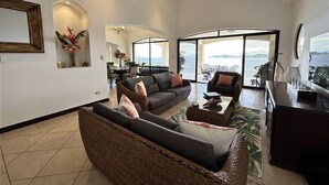 A spacious living room with a large sofa, a coffee table, and a dining area with chairs. - Breathtaking panoramic ocean view Penthouse Condo. (Playa Hermosa)