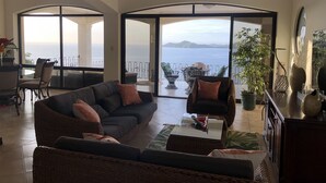 A spacious living room with a large sofa, a coffee table, and a view of the sea through open doors. - Breathtaking panoramic ocean view Penthouse Condo. (Playa Hermosa)