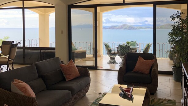 A spacious living room with a large sofa, a coffee table, and a balcony with a view of the sea. - Breathtaking panoramic ocean view Penthouse Condo. (Playa Hermosa)
