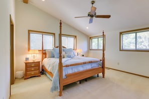 A four-poster bed with a wooden frame and a light blue bedspread, a nightstand with a lamp, and a ceiling fan. - West Virginia Home w/ Deck on Golf Course (Hedgesville)