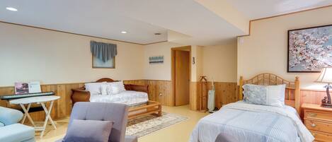 A bedroom with two beds, a wooden headboard, a small table, a chair, and a painting on the wall.