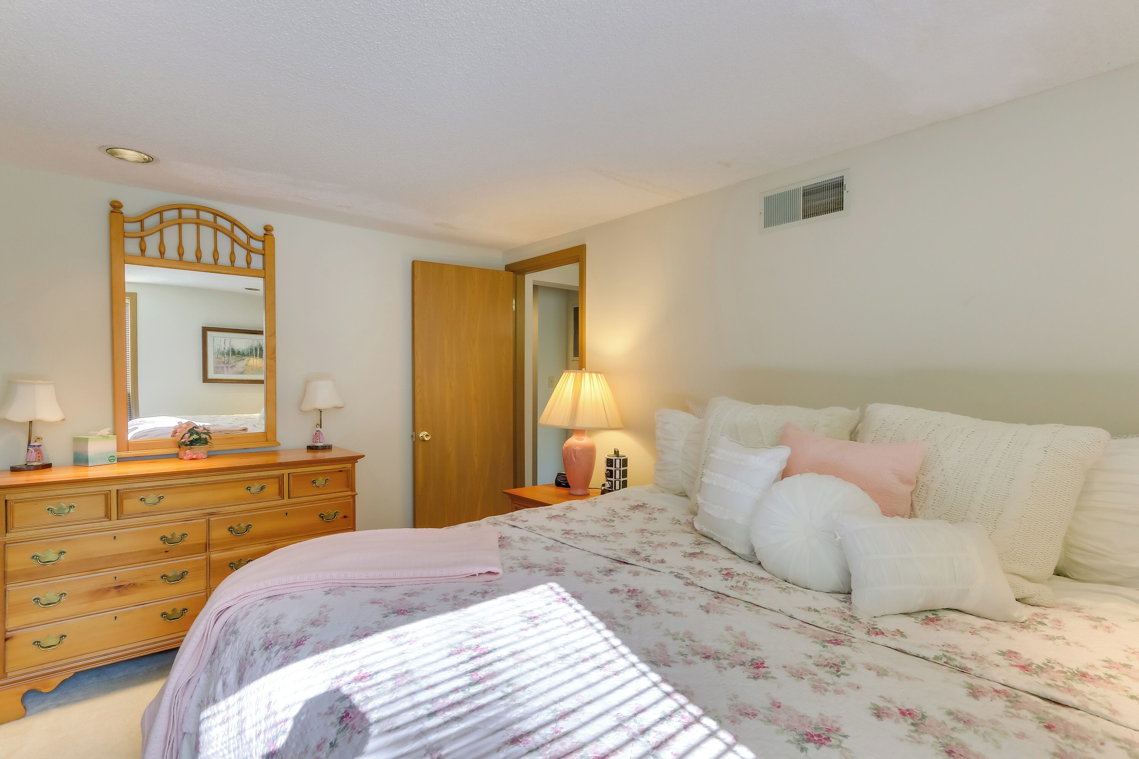 A bedroom with a bed, dresser, mirror, and bedside lamps.