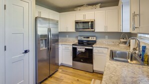 A kitchen with white cabinets, stainless steel appliances, a granite countertop, and a wooden floor. - Family-friendly PCB Vacation Rental, Walk to Beach (Panama City Beach)
