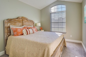 Quarto com cama, mesa de cabeceira, luminária e janela com persianas.