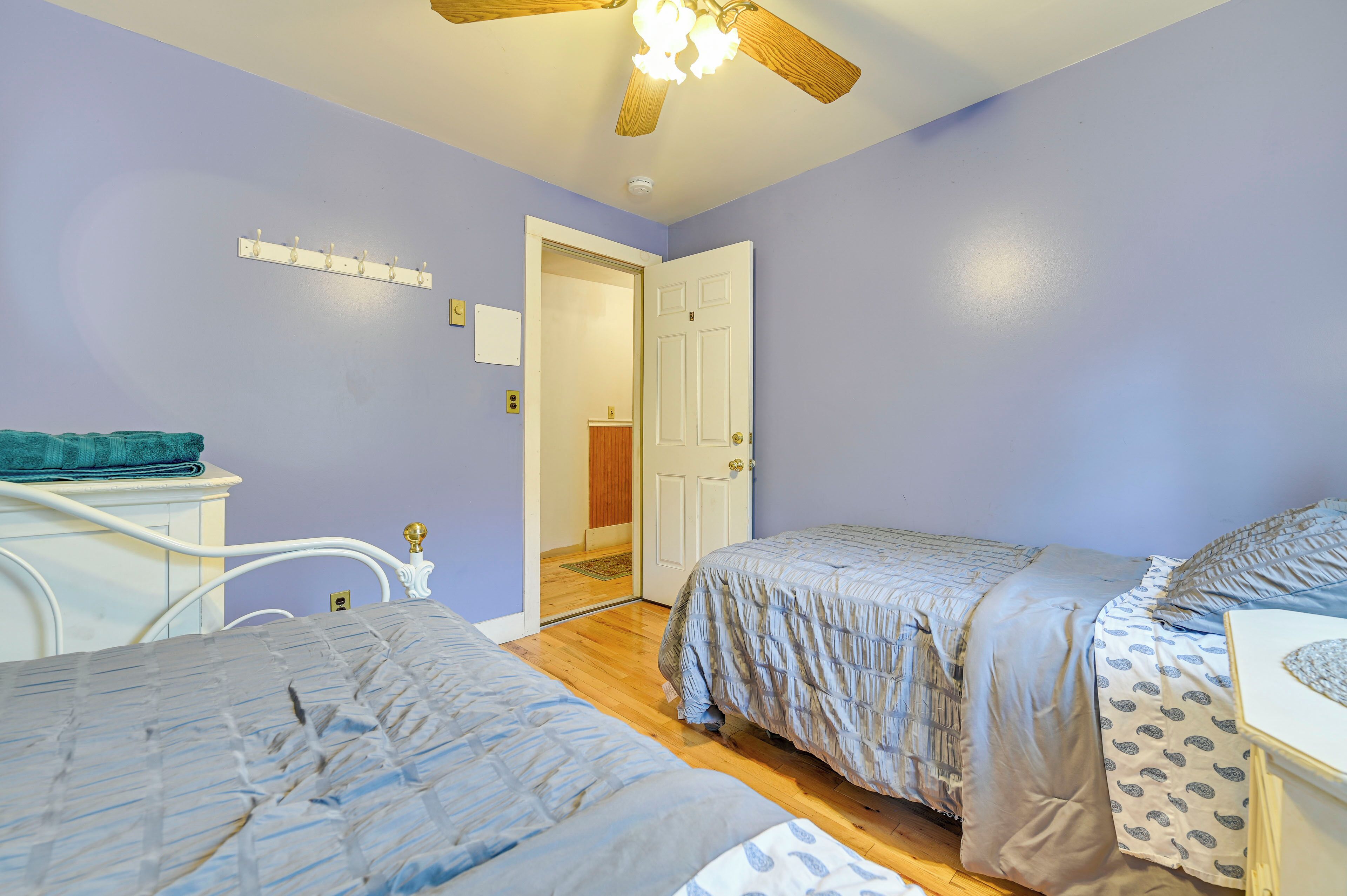 A bedroom with two beds, a white dresser, a ceiling fan, and a door leading to another room.