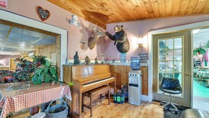 Une pièce chaleureuse avec un plafond en bois, un piano, une tête d’ours fixée au mur et une porte donnant sur l’extérieur.