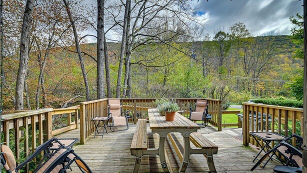 Une terrasse en bois, agrémentée de tables et de chaises pour pique-niquer, entourée d’arbres et offrant une vue sur un paysage vallonné.