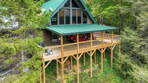 A cabin with a green roof, wooden deck, and a large window overlooking the forest. - Robbinsville Vacation Rental w/ Covered Balcony (Robbinsville)