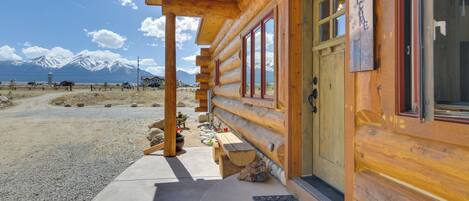 A log cabin with a wooden exterior, a porch, and a view of snow-capped mountains.