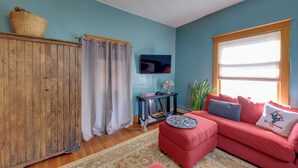 Ein Wohnzimmer mit Holzschrank, rotem Sofa, Fernseher und einem Fenster mit Jalousien.