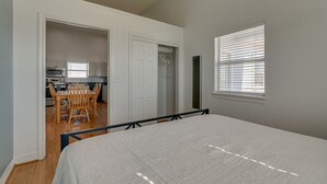 A bedroom with a bed, a window with blinds, a door leading to a kitchen, and a dining area with chairs and a table. - Waterfront Sargent Home w/ Kayaks & Boat Dock! (Bay City)