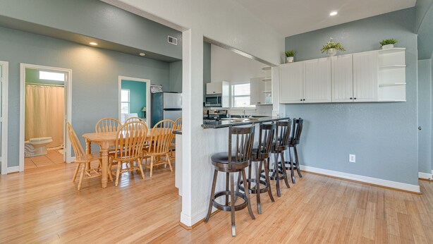 A modern kitchen with white cabinets, a central island with bar stools, and a dining area with wooden chairs. - Waterfront Sargent Home w/ Kayaks & Boat Dock! (Bay City)