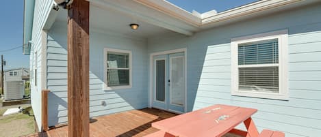 A light blue house with a wooden deck, a pink picnic table, and a door with a glass panel.