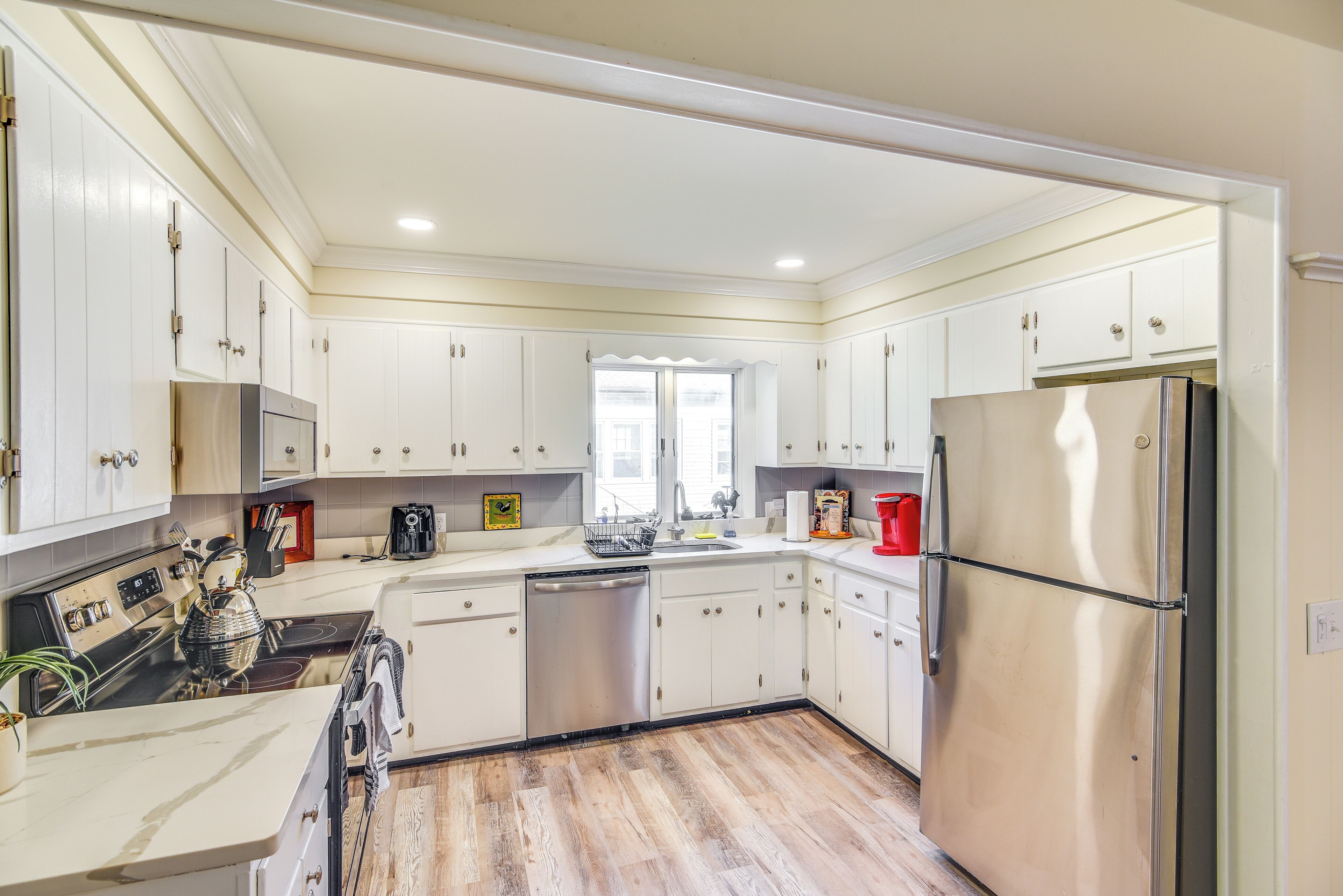A modern kitchen with white cabinets, stainless steel appliances, and a wooden floor.