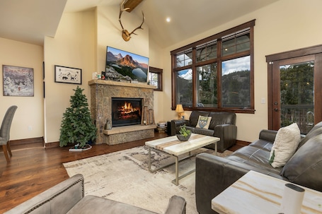 A living room with a fireplace, a Christmas tree, leather sofas, and large windows offering a mountain view.