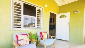 A room with two wooden chairs and a small table, a window with blinds, and a door with a 'hello' sign. - 3BR*Near Beach | Airport Shuttle | Pools | Tennis🌴 (Falmouth)