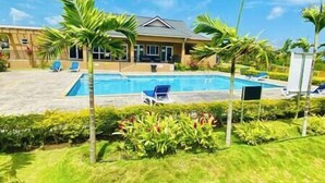 A pool area with a house in the background, surrounded by palm trees and greenery. - 3BR*Near Beach | Airport Shuttle | Pools | Tennis🌴 (Falmouth)