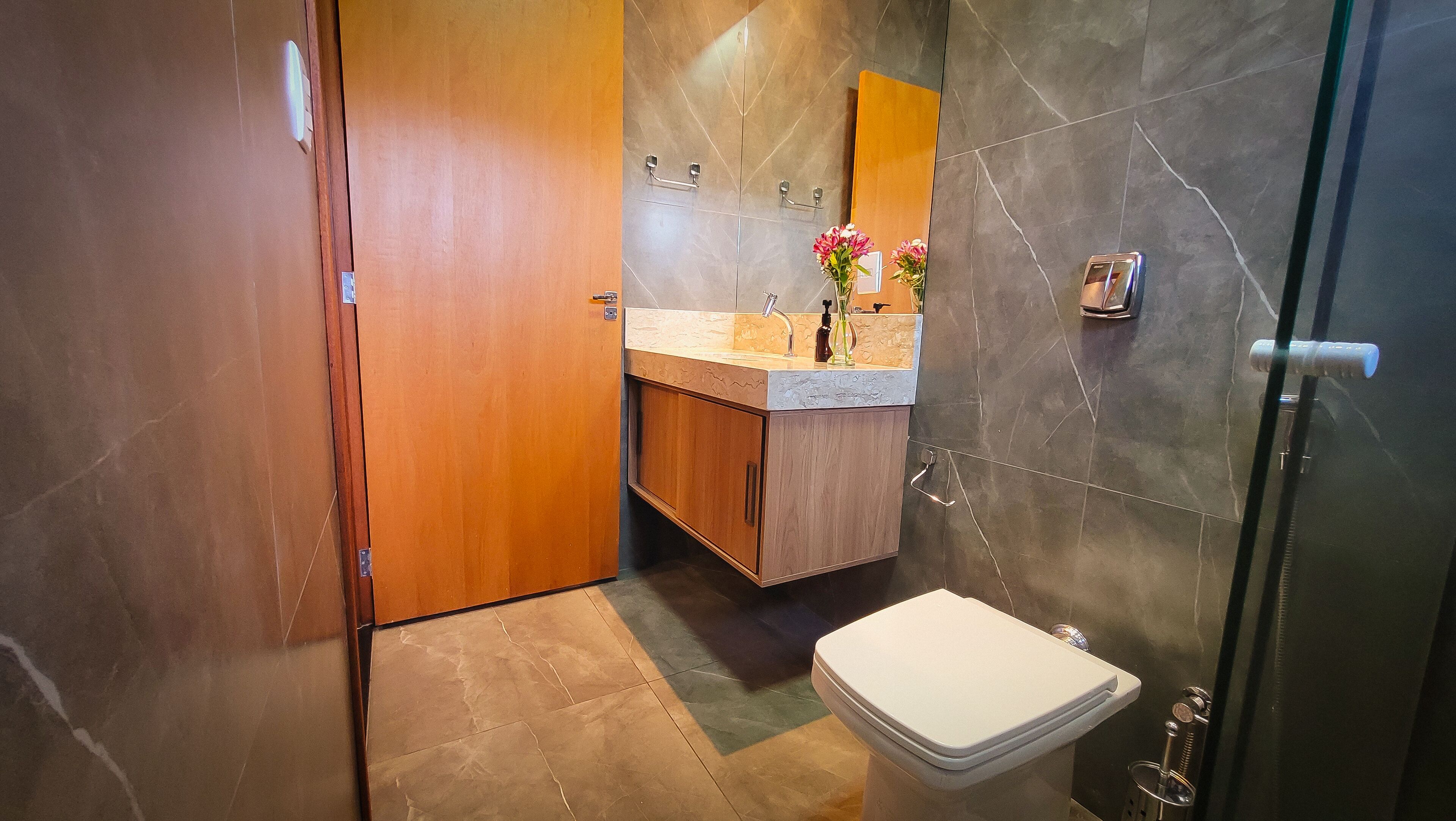 Ein Badezimmer mit Holztür, Waschbecken mit Spiegel, Toilette und Duschbereich.