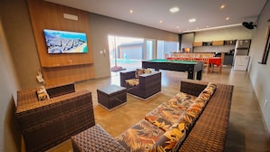 Un salon moderne doté d’une table de billard, de sièges confortables, d’un téléviseur et d’un coin cuisine.