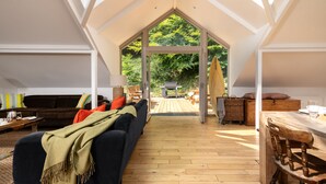 Un loft spacieux avec de hauts plafonds et de grandes fenêtres, un coin salon confortable avec un canapé et des fauteuils, et une table à manger en bois.