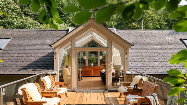 Une terrasse en bois avec des sièges extérieurs et une structure fermée par des parois de verre.