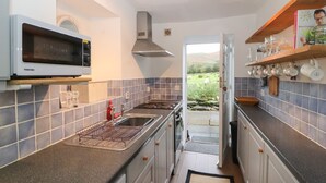 Een moderne keuken met een magnetron, fornuis en spoelbak. Er is uitzicht op een groen landschap door een geopende deur.