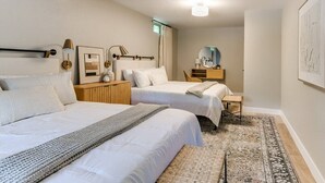 A bedroom with two beds, a bedside table, a nightstand, a lamp, a mirror, and a rug.
