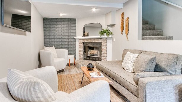 A modern living room with a fireplace, white sofas, and a staircase in the background.
