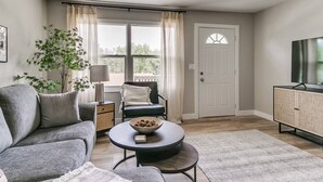 A living room with a sofa, a round coffee table, a chair, a side table, a lamp, a plant, and a television.