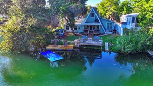 A house with a dock extending into a calm body of water, surrounded by lush greenery. - Weeki Wachee Waterfront-A Frame Stream Dream Cabin (Spring Hill)