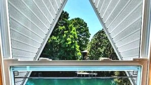 A view through a triangular window with a pool in the foreground and trees in the background. - Weeki Wachee Waterfront-A Frame Stream Dream Cabin (Spring Hill)
