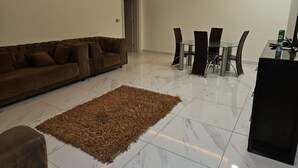 A living room with a brown sofa, a glass dining table with chairs, and a small rug. - Kams homes (Abuja)