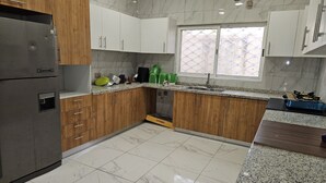 A kitchen with wooden cabinets, a stainless steel refrigerator, a sink, and a stove. - Kams homes (Abuja)