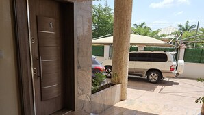 A modern entrance with a wooden door marked '1', a tiled floor, and a covered outdoor area with a parked vehicle. - Kams homes (Abuja)