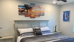 A bedroom with a bed, nightstands, a ceiling fan, and artwork on the walls.