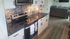 A modern kitchen with a stainless steel microwave, a built-in oven, and a dishwasher. There is a tiled backsplash and a wooden countertop. A ceiling fan and a flat-screen TV are visible in the background.