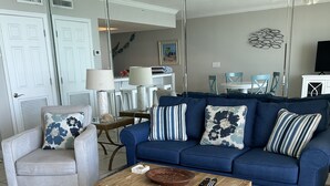 A living room with a blue sofa, a wooden coffee table, a white armchair, and a large mirror reflecting the room.