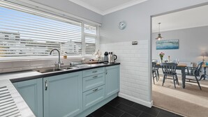 A modern kitchen with light blue cabinets, a black countertop, and a window with blinds.