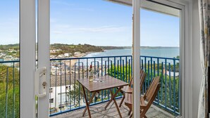 A balcony with a wooden table and chairs, overlooking a beach and ocean.