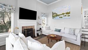 A modern living room with a fireplace, white sofas, a coffee table, and a large flat-screen TV. - Linkside Court 21 - Community Tennis/Pickleball! (Isle of Palms)