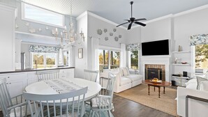 A spacious living area with a fireplace, a dining table, and a TV mounted on the wall. - Linkside Court 21 - Community Tennis/Pickleball! (Isle of Palms)