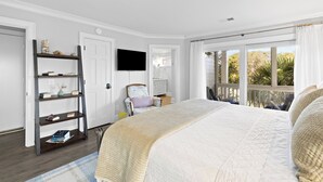 A bedroom with a large bed, a TV, a bookshelf, and a view of the outdoors. - Linkside Court 21 - Community Tennis/Pickleball! (Isle of Palms)