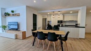 A modern kitchen with white cabinets, a wooden dining table, and black chairs. - Hydros Ter Ripoll HUT (Ripoll)