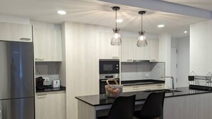A modern kitchen with a stainless steel refrigerator, a built-in oven, and a black countertop. There are two black bar stools and a fruit bowl on the island. - Hydros Ter Ripoll HUT (Ripoll)