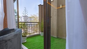 Ein Balkon mit Kunstrasen, einem Blumentopf und Blick auf ein Gebäude im Hintergrund.