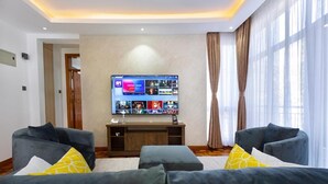 Ein modernes Wohnzimmer mit einem großen Flachbildfernseher an der Wand, zwei grauen Sofas mit gelben Kissen und einer Holz-Unterhaltungsanlage.