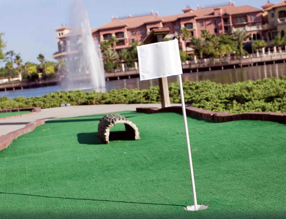 Un parcours de mini-golf avec un green d’entraînement, une arche en pierre et une fontaine en arrière-plan.
